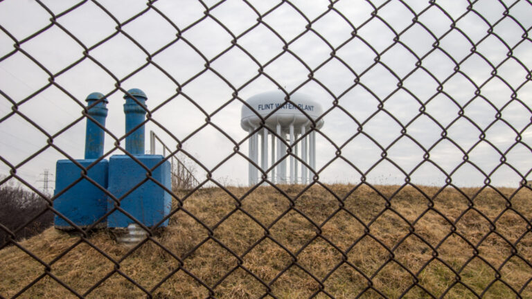 Water tower of Flint Michigan through a chain linked fence