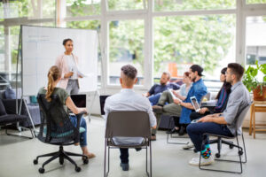 An instructor standing at a whiteboard addressing a small circle of seated students